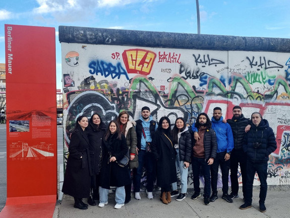 Deltagare på studieresa i Berlin. På bilden står de ute, framför en graffittivägg, och pratar med varandra.