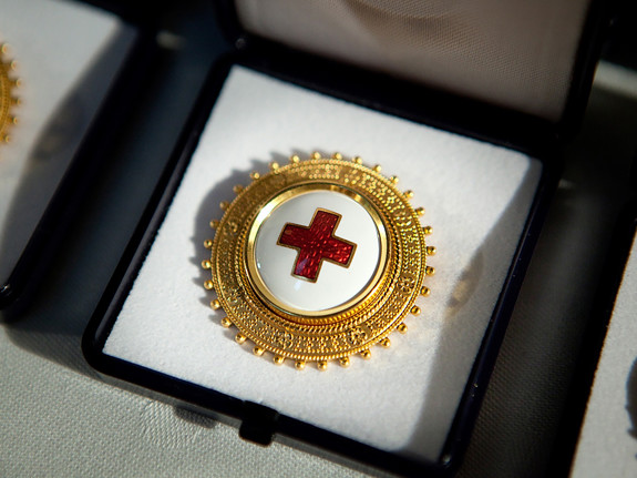 En brosch med Röda Korsets symbol i mitten på vit botten och en kant av guld. Broschen ligger i ett fodral på ett bord.