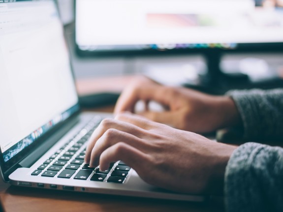 Närbild på en laptop och två händer som skriver på tangentbordet.