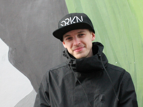 Kille i svart keps och jacka framför en ljusgrön fond