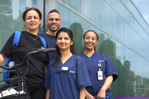 Fyra personer, tre kvinnor och en man, står i en grupp. En kvinna håller i en cykel. De har alla hemtjänstkläder på sig och tittar in i kameran