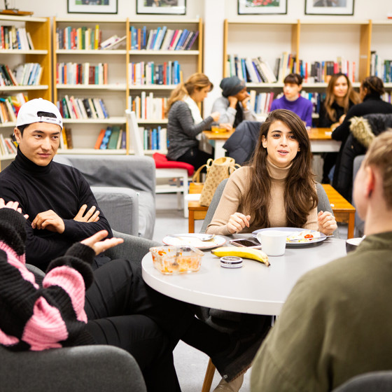 Deltagare sitter runt olika bord i skolans bibliotek och diskuterar