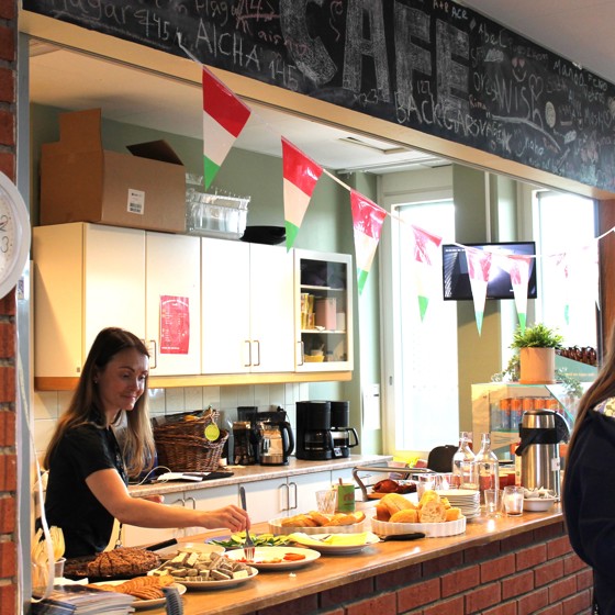 Två kvinnliga unga volontärer i långt brunt hår förbereder en buffé med kaffe och hembakat bröd till dagens seniorverksamhet.