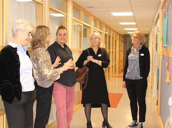 Fem kvinnor står och samtalar kring en utställning i en korridor på Röda Korsets folkhögskola