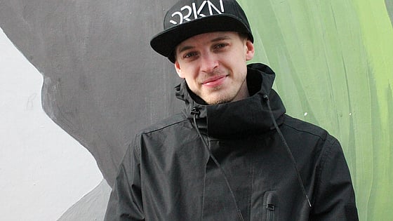 Kille i svart keps och jacka framför en ljusgrön fond