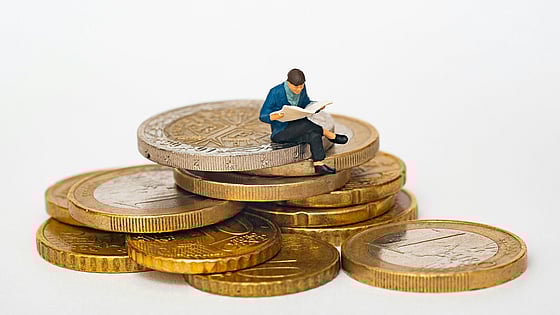 På en trave med mynt sitter en liten docka med korslagda ben och läser i en bok