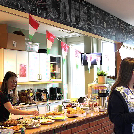 Två kvinnliga unga volontärer i långt brunt hår förbereder en buffé med kaffe och hembakat bröd till dagens seniorverksamhet.