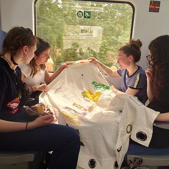 En perrong på en stor järnvägsstation. Till höger står ett rött tvåvåningståg. På perrongen kramar två personer om varandra. Den ena har en resväska bredvid sig.