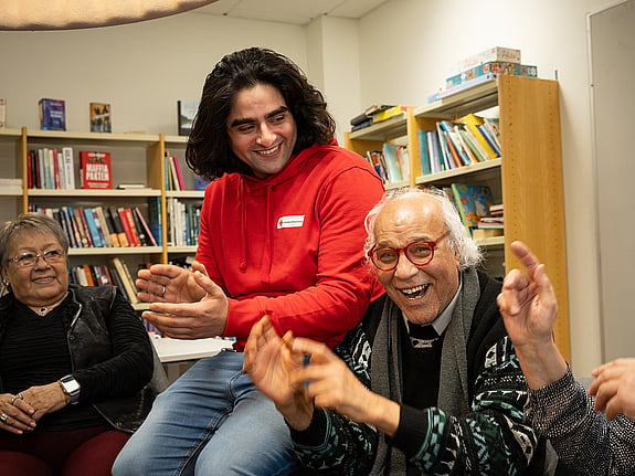 En ung man i Röda Korset tröja klappar händerna tillsammans med några äldre människor
