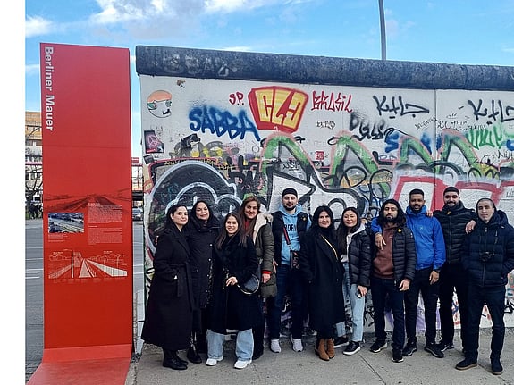 Deltagare på studieresa i Berlin. På bilden står de ute, framför en graffittivägg, och pratar med varandra.