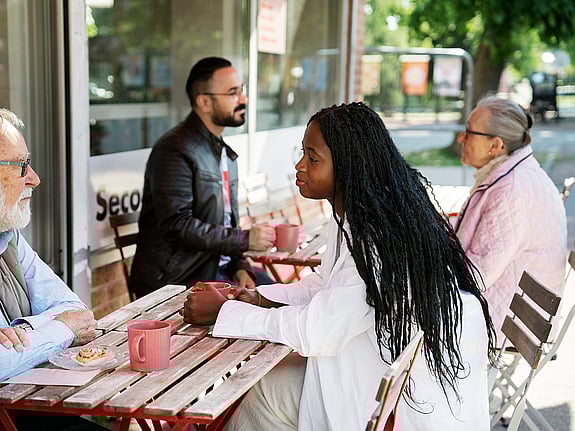 Fyra personer med olika åldrar och bakgrund sitter och samtalar på en uteservering