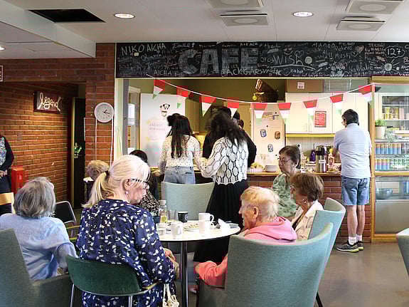 En grupp seniorer sitter runt ett bord och umgås på seniorcaféet arrangerat av Röda Korsets folkhögskolas deltagare.