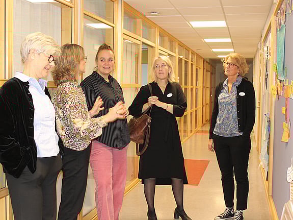 Fem kvinnor står och samtalar kring en utställning i en korridor på Röda Korsets folkhögskola