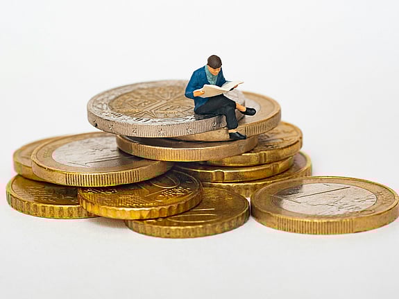 På en trave med mynt sitter en liten docka med korslagda ben och läser i en bok