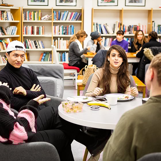 Deltagare sitter runt olika bord i skolans bibliotek och diskuterar