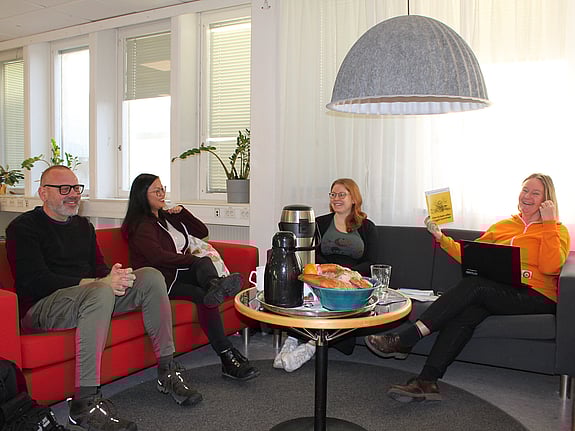 Tre deltagare och en lärare på kursen i krisberedskap sitter och samtalar runt ett bord med fika. En man och en kvinna sitter i en röd soffa och två kvinnor sitter i en grå. De är glada. Läraren håller upp en informationsskrift om krisberedskap.