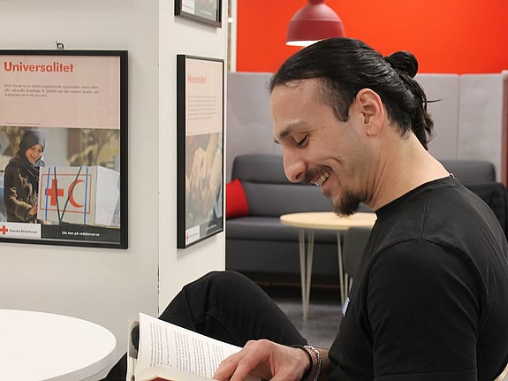 Ung man sitter och tittar ner i en bok. Ser glad ut.