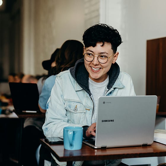 En person i kort hår och jeansjacka sitter vid en dator och pluggar