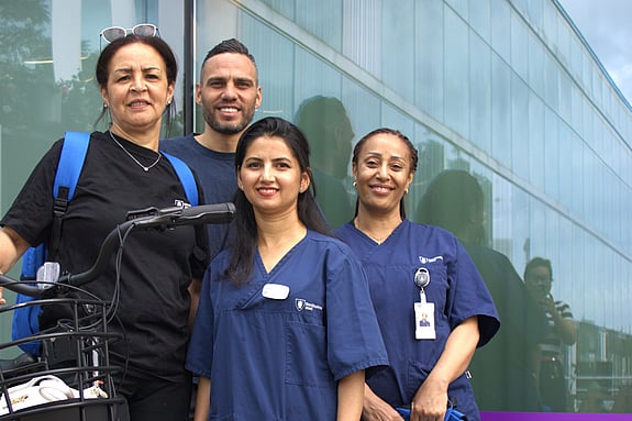 Fyra personer, tre kvinnor och en man, står i en grupp. En kvinna håller i en cykel. De har alla hemtjänstkläder på sig och tittar in i kameran