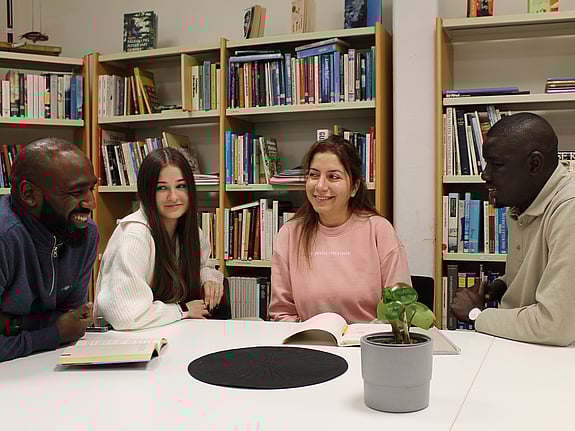 Fyra kursdeltagare sitter i biblioteket och diskuterar ett grupparbete