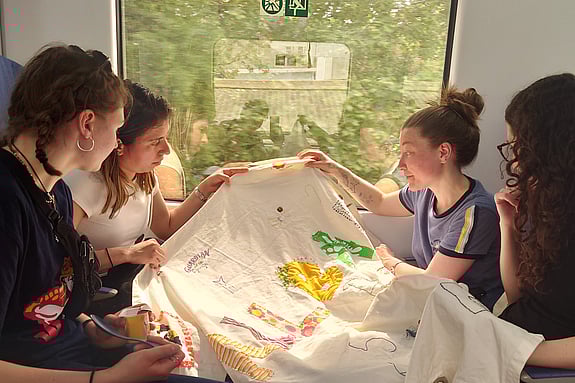 Fyra deltagare på kursen i hållbart resande sitter mittemot varandra på ett tåg och syr på en stor bonad