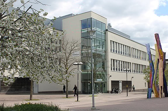 Ett foto av Röda Korsets folkhögskola på Bredholmstorget i Skärholmen. Det är vår i luften och några personer rör sig framför skolan.