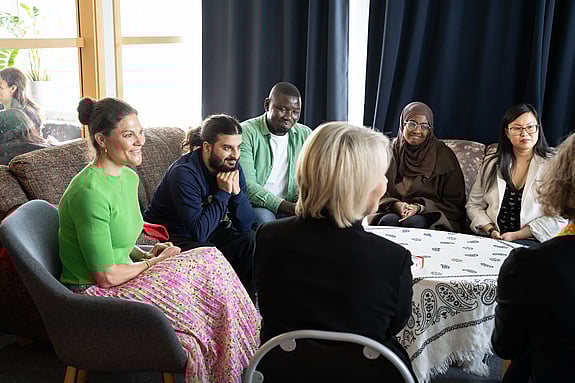 Kronprinsessan Victoria samtalar med deltagare från Röda Korsets folkhögskola. De sitter i en soffgrupp och är glada och intresserade av varandra.