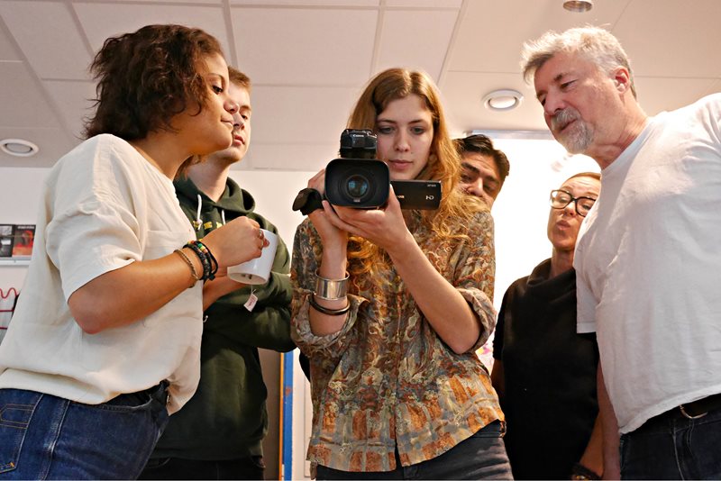 Fem kursdeltagare på filmkursen Dokumentär i världen samlas kring en filmkamera. De tittar nyfiket på displayen. Till höger står kursens lärare i vit t-shirt.