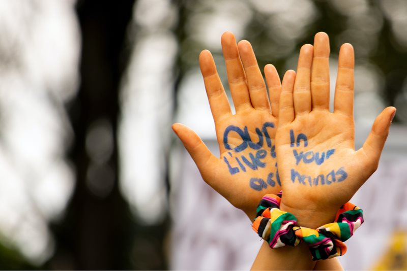 Två händer som korsas. I handflatorna står skrivet med blå text "Our lives in your hands".