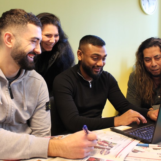 Fyra kursdeltagare i ett klassrum. De samlas kring ett arbete det gjort över en dator och ler