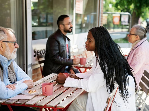 Fyra personer med olika åldrar och bakgrund sitter och samtalar på en uteservering