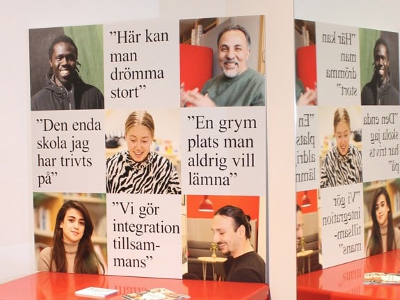 Bilden visar en vägg med en vepa med värdeord för Röda Korsets folkhögskola, en anslagstavla med olika affischer och en röd parksoffa