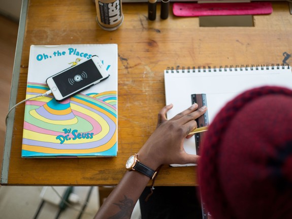 En kille i röd mössa syns bakifrån när han pluggar matte. Närbild på baksida huvud, arm med klocka och skrivbord med telefon och skrivböcker