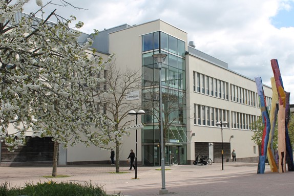 Ett foto av Röda Korsets folkhögskola på Bredholmstorget i Skärholmen. Det är vår i luften och några personer rör sig framför skolan.
